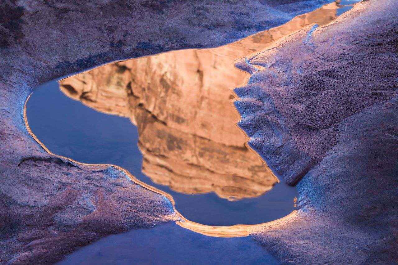 A sandstone wall mirrored in a still desert reflection pool amid pale slickrock near Moab