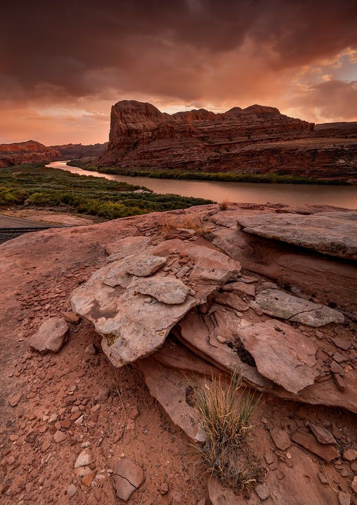 The Colorado River winding beneath red sandstone buttes under a dramatic sunset sky, by Colleen Miniuk
