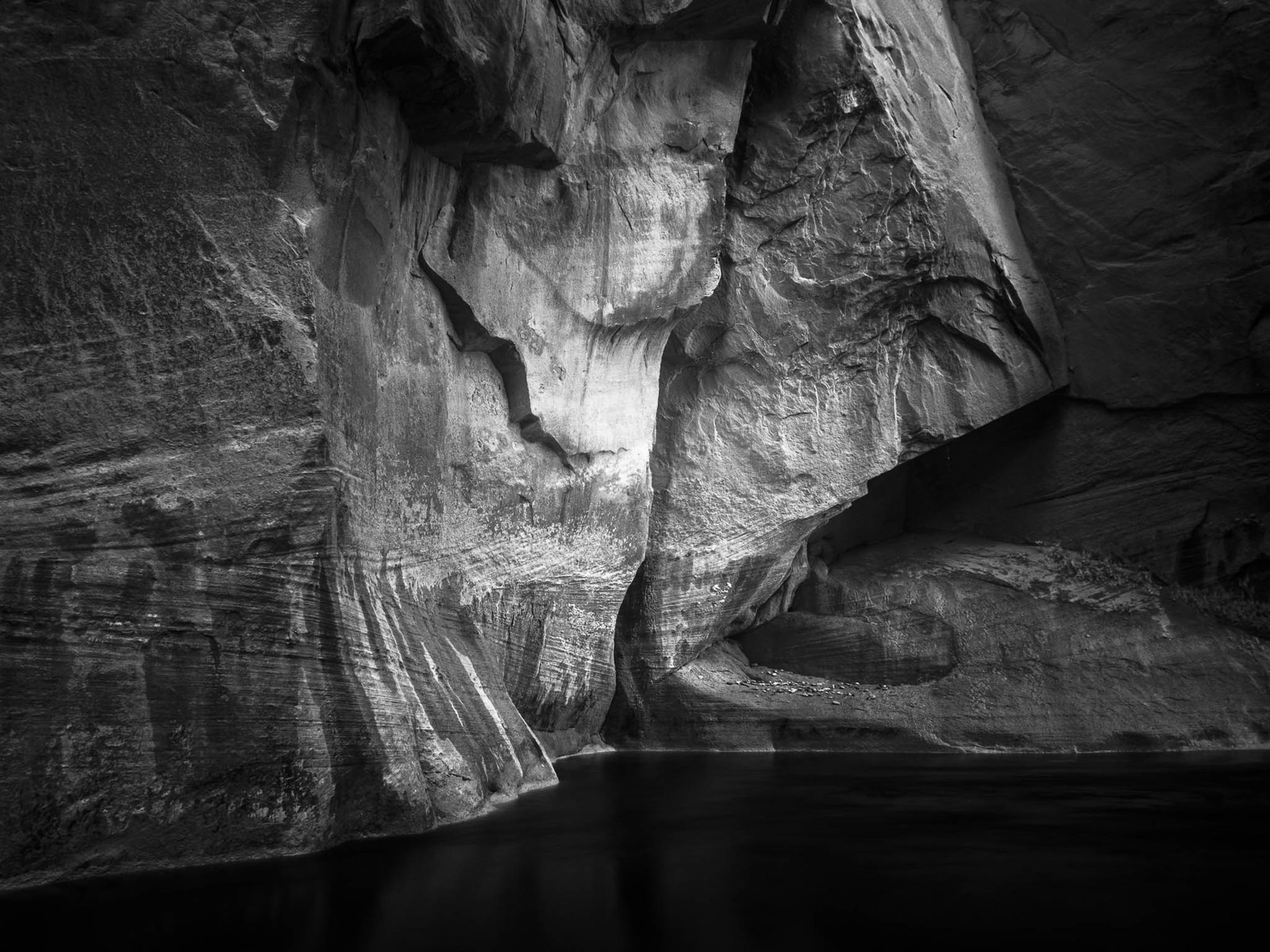 Carved sandstone canyon wall above dark still water, black and white, by David Kingham