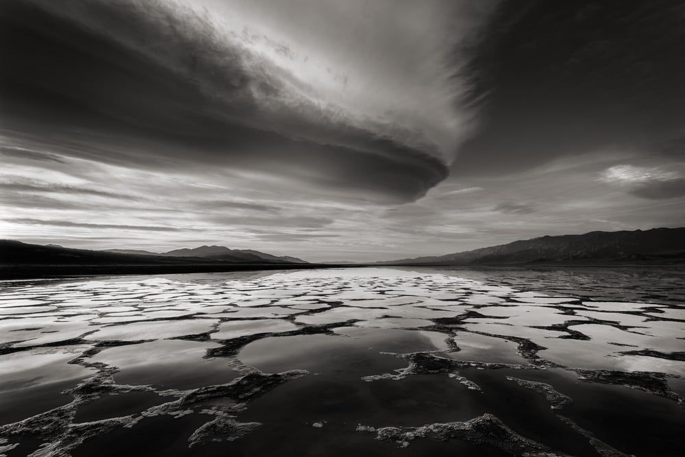 A dramatic lenticular cloud over the reflective salt polygons of a Death Valley playa, black and white, by Michael E. Gordon