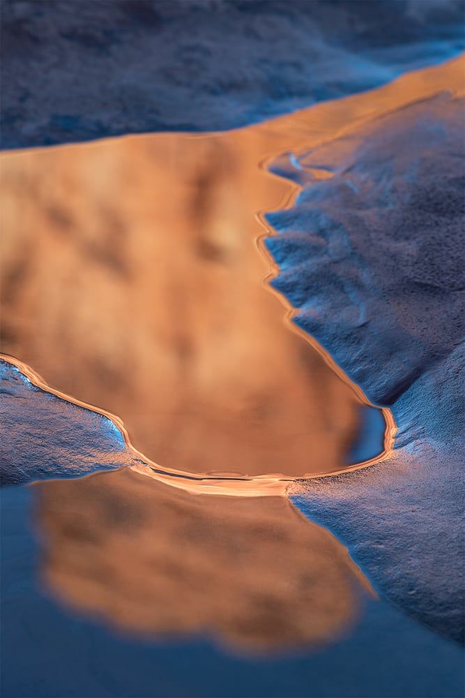 Warm sandstone glowing in the still blue water of a slickrock reflection pool, by Bruce Hucko