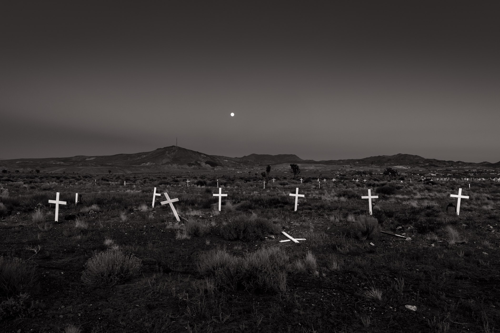 White roadside crosses beneath a rising moon in the high desert, black and white, by Chuck Kimmerle